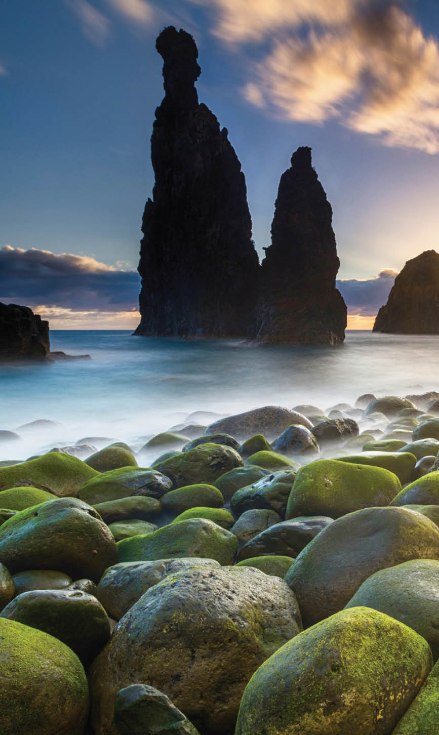 Green stones beach and giant rocks in the ocean at sunrise