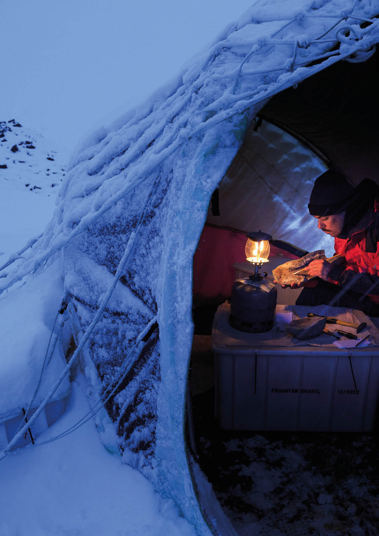 A paleontologist examines a fossil sample under the light of a lamp inside the tent in Antarctica   Location: Vega Island, Antarctica Photographer: Edson Vandeira