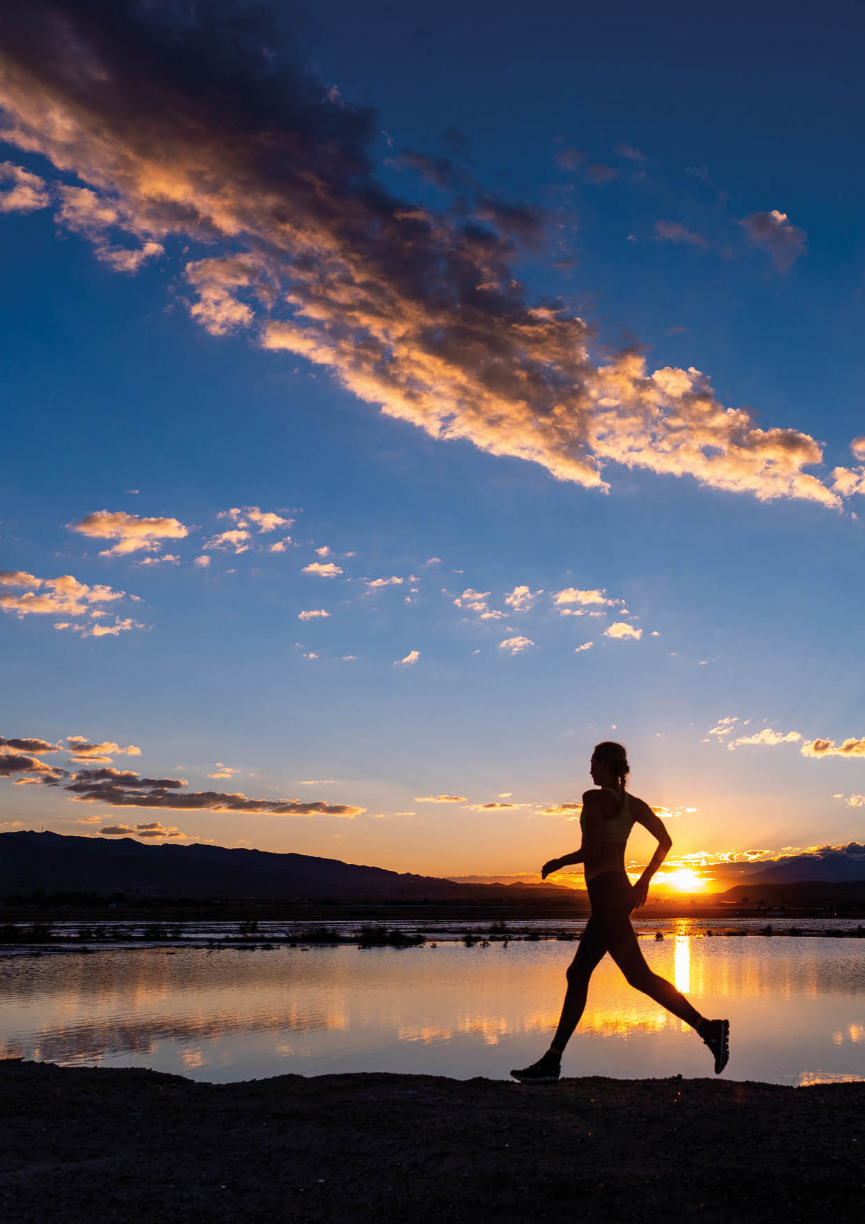 A woman runs along a lake reflecting the sunset   Location: Joshua Tree, Sunfair dry lake bed, California, USA Photographer: Ben Horton