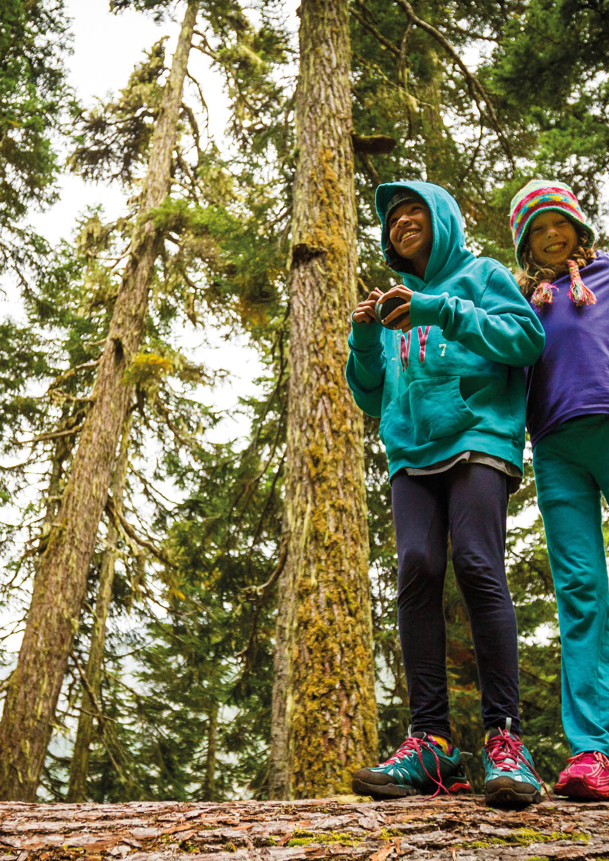 Two young girls enjoy walking along a fallen log in the forest   Location: Washington Photographer: Mark Stone