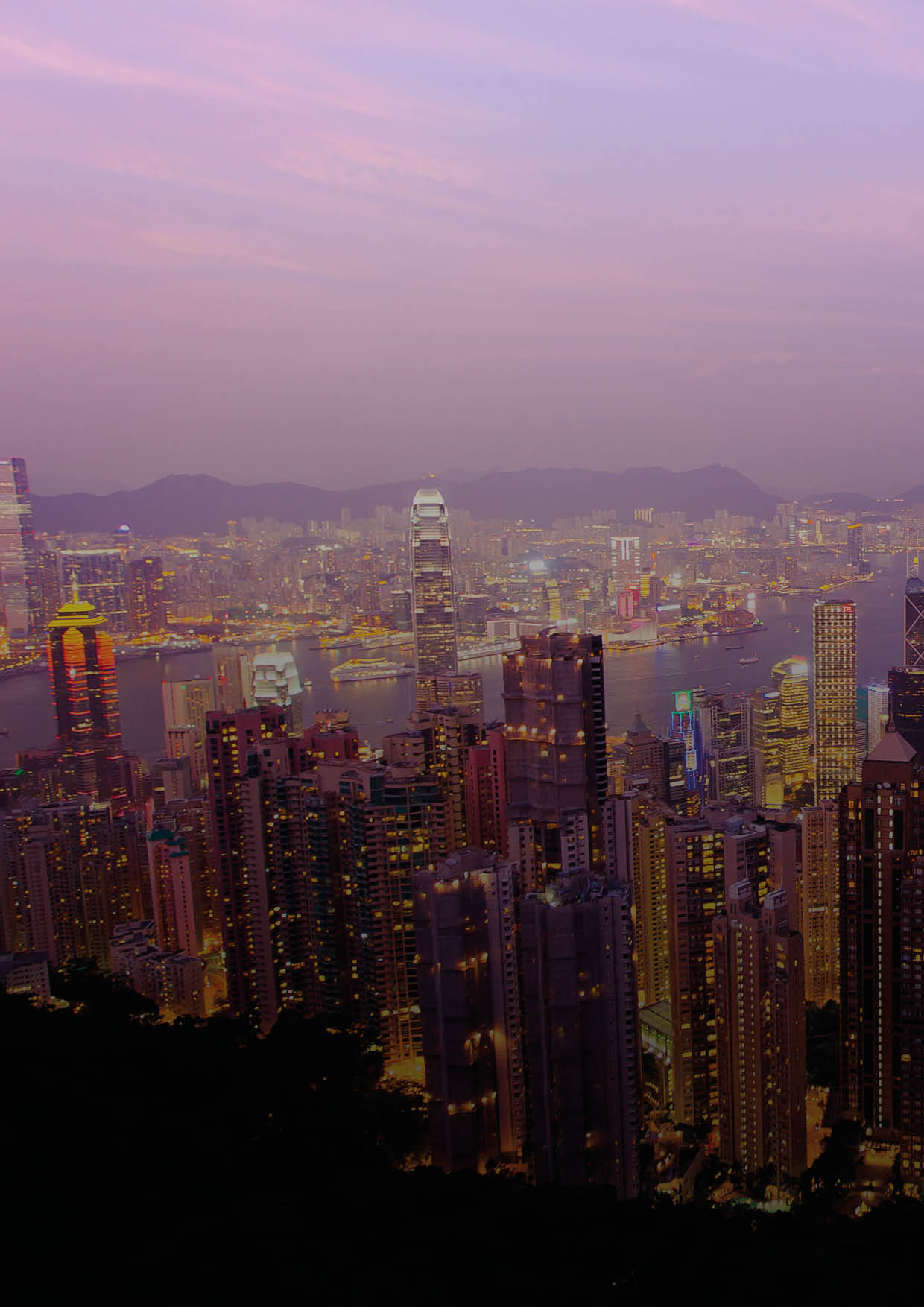 Tourists Photograph the Hong Kong skyline and Victoria Harbor from Victoria Peak at sunset.