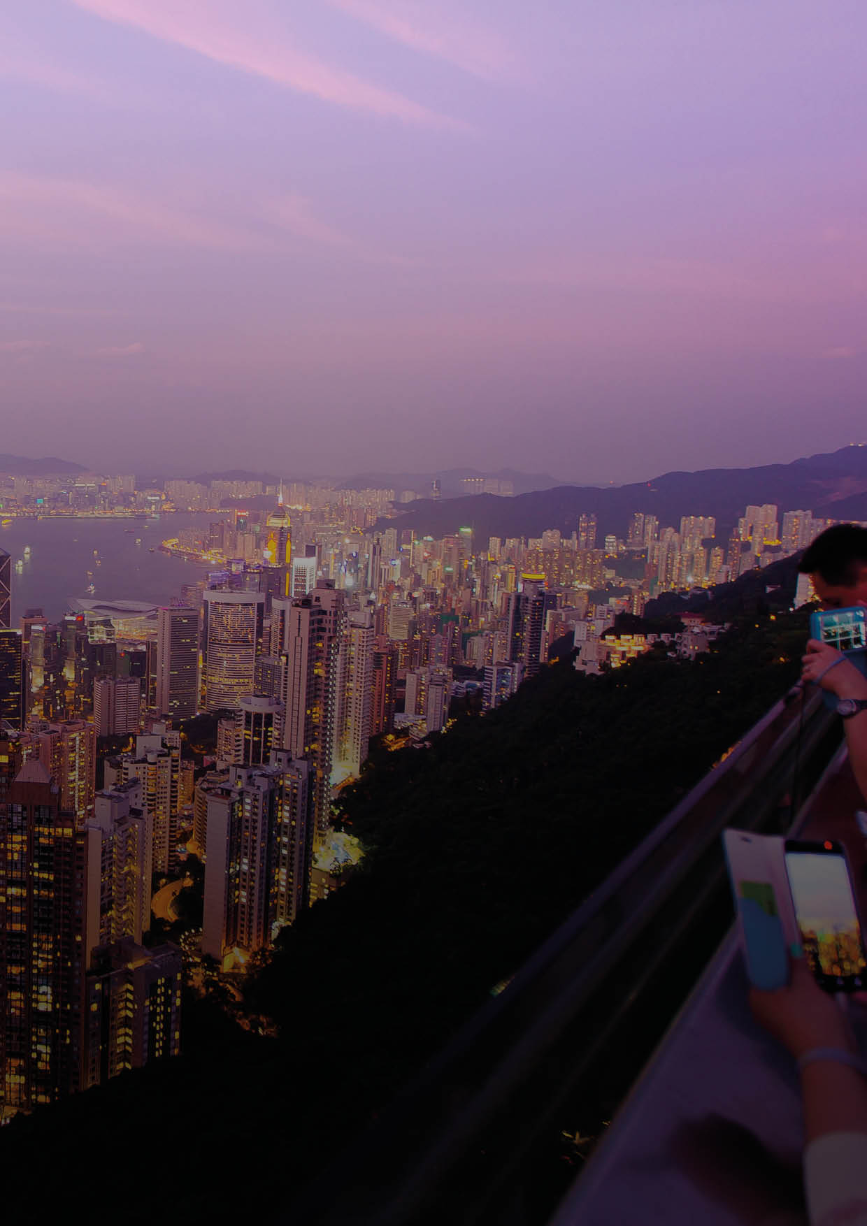 Tourists Photograph the Hong Kong skyline and Victoria Harbor from Victoria Peak at sunset.
