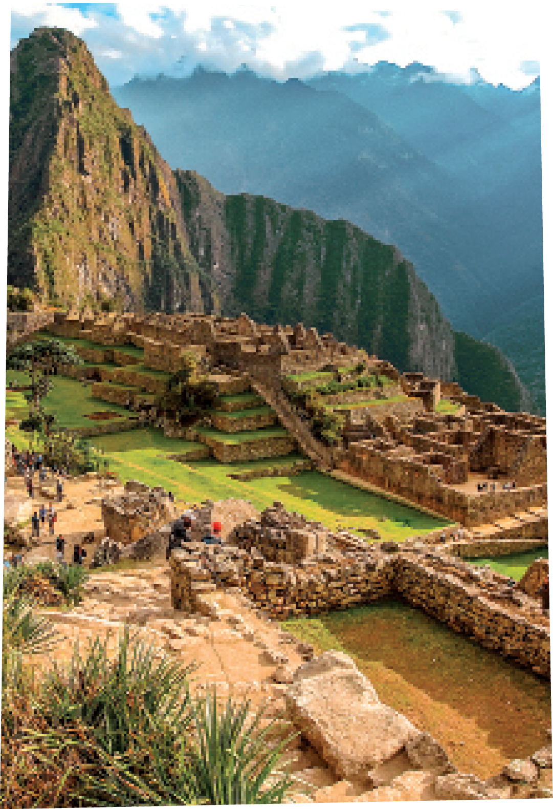 Machu picchu mountain view during sun rise with beautiful light and some tourists in the distance.