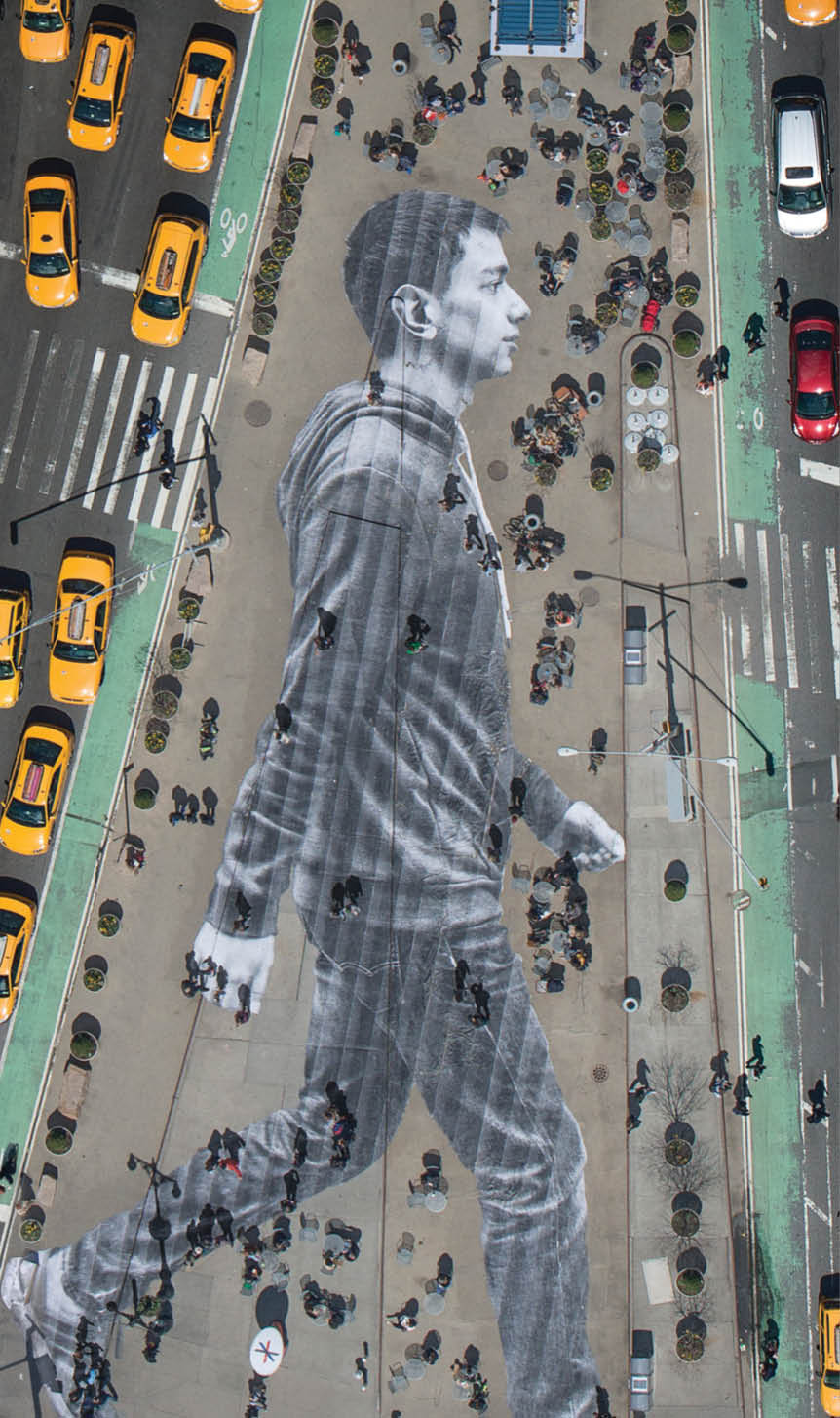 What you see on the cover of this week’s New York Times Magazine is real. The image is by the French artist JR, who is known for pasting giant photographs on urban surfaces all over the world. About six weeks ago, we met with JR to discuss a project for our Walking New York issue. Lately, JR’s work has been preoccupied with the theme of immigration. An installation at Ellis Island features large archival photographs of immigrants displayed throughout the island’s abandoned hospital. For this project, we decided we’d photograph recent immigrants and paste their images on the city’s streets, where they and other immigrants are often invisible. The pasting would be made in the heart of Manhattan, on Flatiron plaza, the triangle of pavement between Fifth Avenue, Broadway and East 23rd Street.  Earlier this month, JR photographed 16 people who arrived in New York within the last year and made their portraits while they walked down the streets of NoLIta. (Some of these portraits can been seen here.) For the cover, we zeroed in on Elmar Aliyev, a 20-year-old waiter at Old Baku, an Azerbaijani restaurant on Ditmas Avenue in Brooklyn. Elmar immigrated to the United States from Azerbaijan last August after he won the green-card lottery. He likes to walk in Central Park and around the Plaza, locations from his favorite movie, “Home Alone 2.” JR liked the way Aliyev swung his arms when he walked.  Aliyev’s picture was then printed on 62 strips of paper. On April 11, JR and his 20-person crew took these strips to Flatiron plaza and began affixing them to the ground at 4 a.m. The pasting took about three and a half hours and resulted in a 150-foot-tall image of Aliyev striding eastward. The sun came up. Pedestrians began to wander over Aliyev. Just as JR had predicted, they often walked right over him without even noticing.  To make out the image, you had to be high above. In the middle of the day, when the angles of shadow were favorable, JR went up in a helicopter and photographed the pasting, with all the cheerful and untidy street life of an early spring day in New York City happening on and around it.  That image is the one you see on the cover of the magazine — a gloriously massive portrait of one of the city’s 3.1 million immigrants, unseen by many of the people passing him on the street.