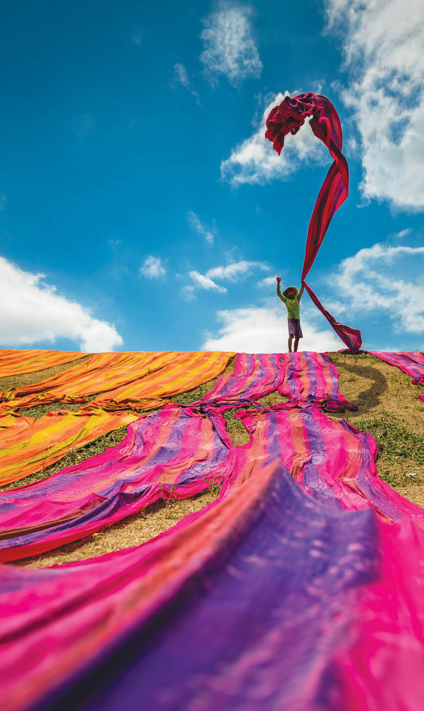 Long rolls of traditional fabric rolled down a hill to dry in the sun, creating a sea of color, Indonesia. ©Chue Ardi RH 1A and 1B cover image