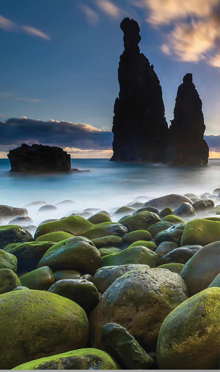 Green stones beach and giant rocks in the ocean at sunrise