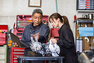 Father and daughter working on repairing a motorcycle engine together using a laptop computer