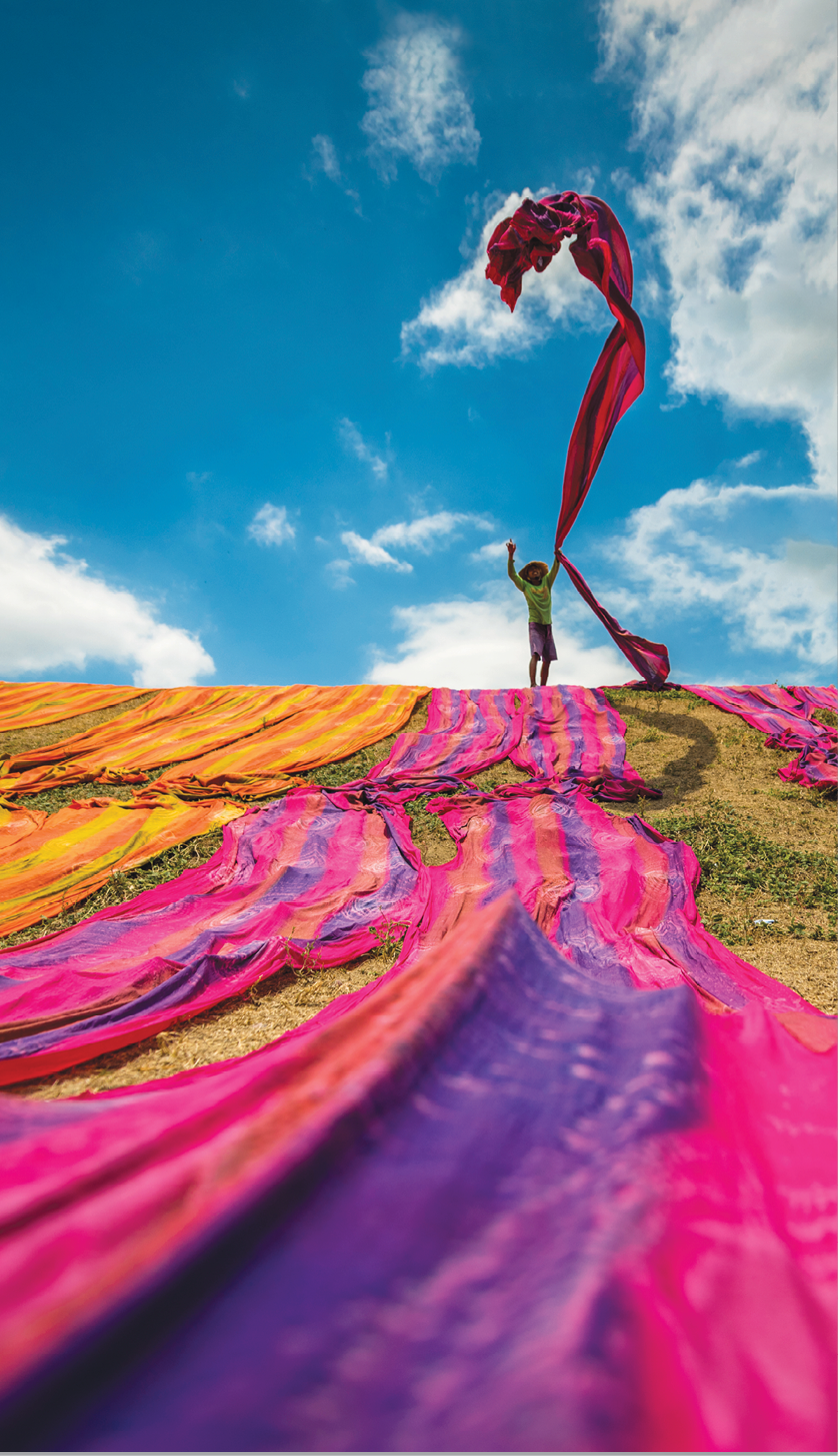 Long rolls of traditional fabric rolled down a hill to dry in the sun, creating a sea of color, Indonesia. ©Chue Ardi RH 1A and 1B cover image