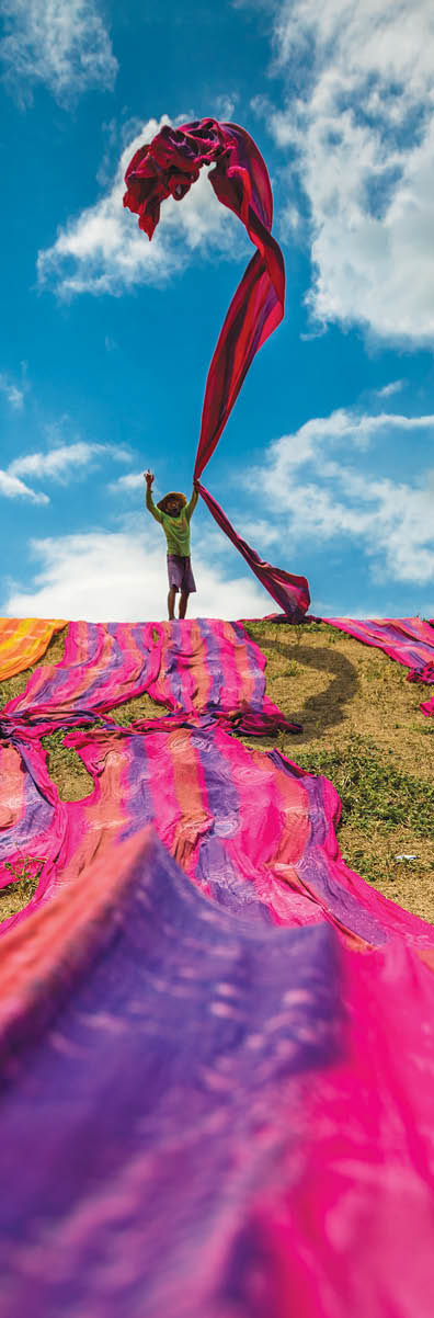 Long rolls of traditional fabric rolled down a hill to dry in the sun, creating a sea of color, Indonesia. ©Chue Ardi RH 1A and 1B cover image