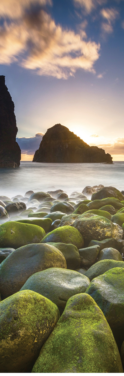 Green stones beach and giant rocks in the ocean at sunrise