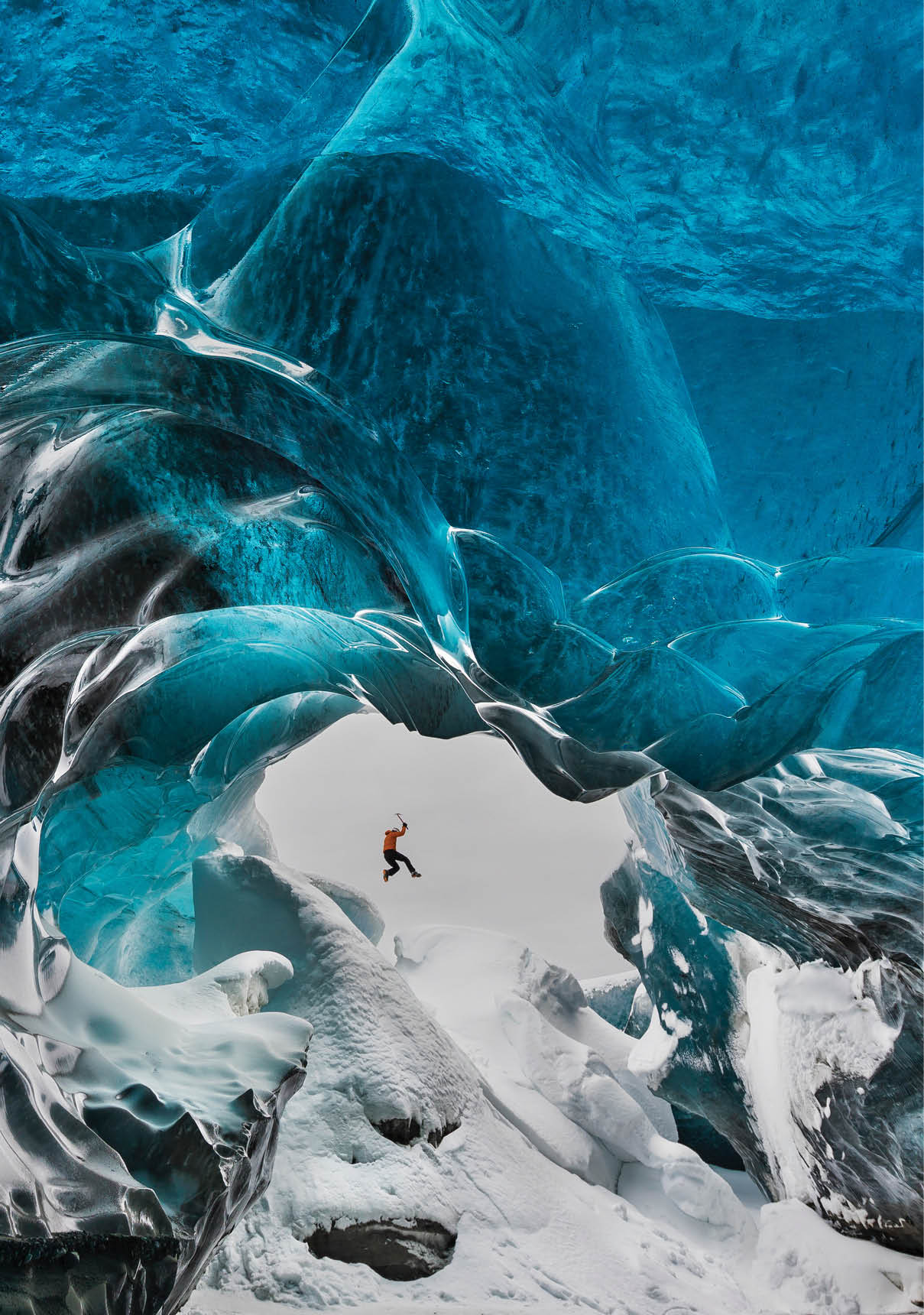 Man jumping across piles of snow in Crystal Cave of Vatnajokull ice cap, Iceland