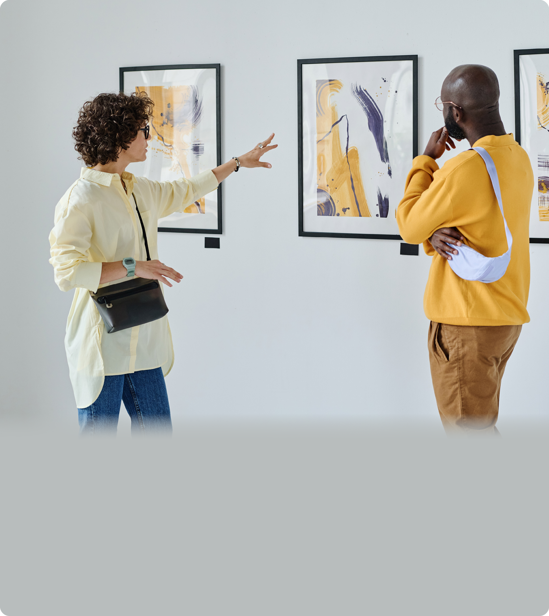 Young woman discussing paintings on wall together with African man while they visiting art gallery