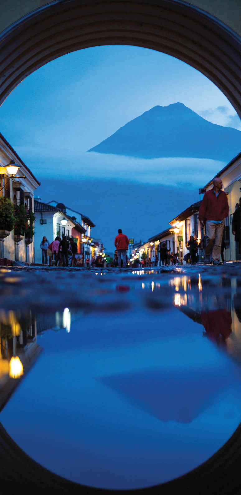 “Twin Peaks of Antigua”. The shadow of night is cast over Antigua as Volc n de Agua's silhouette dominates the horizon through Santa Catalina Arch, reflecting in the cobblestone rain puddles. Photo location: Santa Catalina Arch, Antigua, Guatemala. (Photo and caption by Beau Pilgrim/National Geographic Photo Contest)