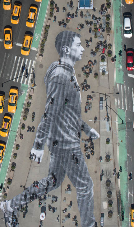 What you see on the cover of this week’s New York Times Magazine is real. The image is by the French artist JR, who is known for pasting giant photographs on urban surfaces all over the world. About six weeks ago, we met with JR to discuss a project for our Walking New York issue. Lately, JR’s work has been preoccupied with the theme of immigration. An installation at Ellis Island features large archival photographs of immigrants displayed throughout the island’s abandoned hospital. For this project, we decided we’d photograph recent immigrants and paste their images on the city’s streets, where they and other immigrants are often invisible. The pasting would be made in the heart of Manhattan, on Flatiron plaza, the triangle of pavement between Fifth Avenue, Broadway and East 23rd Street.  Earlier this month, JR photographed 16 people who arrived in New York within the last year and made their portraits while they walked down the streets of NoLIta. (Some of these portraits can been seen here.) For the cover, we zeroed in on Elmar Aliyev, a 20-year-old waiter at Old Baku, an Azerbaijani restaurant on Ditmas Avenue in Brooklyn. Elmar immigrated to the United States from Azerbaijan last August after he won the green-card lottery. He likes to walk in Central Park and around the Plaza, locations from his favorite movie, “Home Alone 2.” JR liked the way Aliyev swung his arms when he walked.  Aliyev’s picture was then printed on 62 strips of paper. On April 11, JR and his 20-person crew took these strips to Flatiron plaza and began affixing them to the ground at 4 a.m. The pasting took about three and a half hours and resulted in a 150-foot-tall image of Aliyev striding eastward. The sun came up. Pedestrians began to wander over Aliyev. Just as JR had predicted, they often walked right over him without even noticing.  To make out the image, you had to be high above. In the middle of the day, when the angles of shadow were favorable, JR went up in a helicopter and photographed the pasting, with all the cheerful and untidy street life of an early spring day in New York City happening on and around it.  That image is the one you see on the cover of the magazine — a gloriously massive portrait of one of the city’s 3.1 million immigrants, unseen by many of the people passing him on the street.