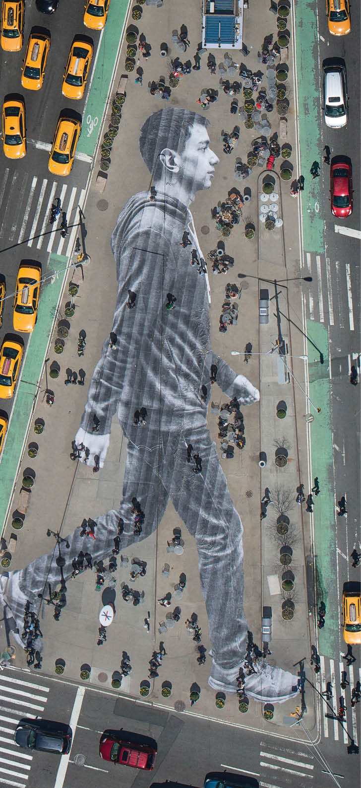 What you see on the cover of this week s New York Times Magazine is real  The image is by the French artist JR, who is known for pasting giant photographs on urban surfaces all over the world  About six weeks ago, we met with JR to discuss a project for our Walking New York issue  Lately, JR s work has been preoccupied with the theme of immigration  An installation at Ellis Island features large archival photographs of immigrants displayed throughout the island s abandoned hospital   For this project, we decided we d photograph recent immigrants and paste their images on the city s streets, where they and other immigrants are often invisible  The pasting would be made in the heart of Manhattan, on Flatiron plaza, the triangle of pavement between Fifth Avenue, Broadway and East 23rd Street   Earlier this month, JR photographed 16 people who arrived in New York within the last year and made their portraits while they walked down the streets of NoLIta  (Some of these portraits can been seen here ) For the cover, we zeroed in on Elmar Aliyev, a 20-year-old waiter at Old Baku, an Azerbaijani restaurant on Ditmas Avenue in Brooklyn  Elmar immigrated to the United States from Azerbaijan last August after he won the green-card lottery  He likes to walk in Central Park and around the Plaza, locations from his favorite movie,  Home Alone 2   JR liked the way Aliyev swung his arms when he walked   Aliyev s picture was then printed on 62 strips of paper  On April 11, JR and his 20-person crew took these strips to Flatiron plaza and began affixing them to the ground at 4 a m  The pasting took about three and a half hours and resulted in a 150-foot-tall image of Aliyev striding eastward  The sun came up  Pedestrians began to wander over Aliyev  Just as JR had predicted, they often walked right over him without even noticing   To make out the image, you had to be high above  In the middle of the day, when the angles of shadow were favorable, JR went up in a helicopter and photographed the pasting, with all the cheerful and untidy street life of an early spring day in New York City happening on and around it   That image is the one you see on the cover of the magazine — a gloriously massive portrait of one of the city s 3 1 million immigrants, unseen by many of the people passing him on the street 