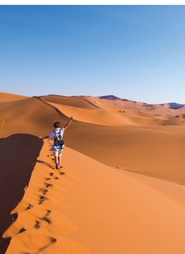 Tourist walking on the scenic dunes of Sossusvlei, Namib desert, Namib Naukluft National Park, Namibia. Afternoon light. Adventure and exploration in Africa.
