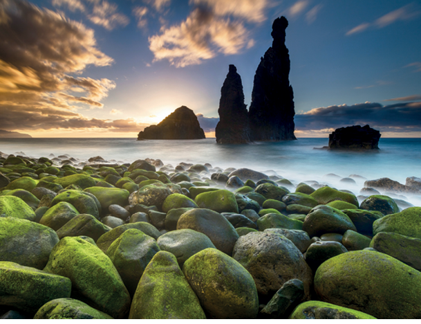 Green stones beach and giant rocks in the ocean at sunrise