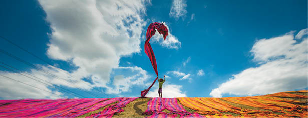 Long rolls of traditional fabric rolled down a hill to dry in the sun, creating a sea of color, Indonesia. ©Chue Ardi RH 1A and 1B cover image