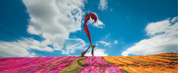 Long rolls of traditional fabric rolled down a hill to dry in the sun, creating a sea of color, Indonesia. ©Chue Ardi RH 1A and 1B cover image