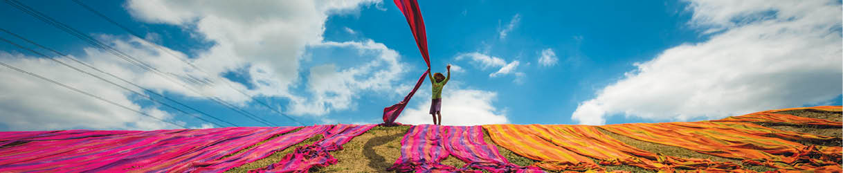 Long rolls of traditional fabric rolled down a hill to dry in the sun, creating a sea of color, Indonesia. ©Chue Ardi RH 1A and 1B cover image