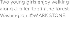 Two young girls enjoy walking along a fallen log in the forest. Washington. ©MARK STONE 